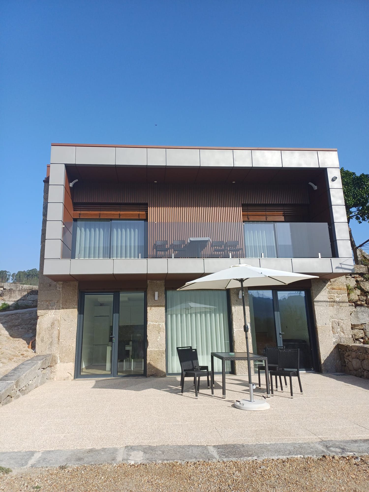 A modern two-story building with a balcony, outdoor seating, and a clear sky.