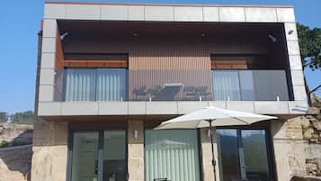 A modern two-story building with a balcony, outdoor seating, and a clear sky.