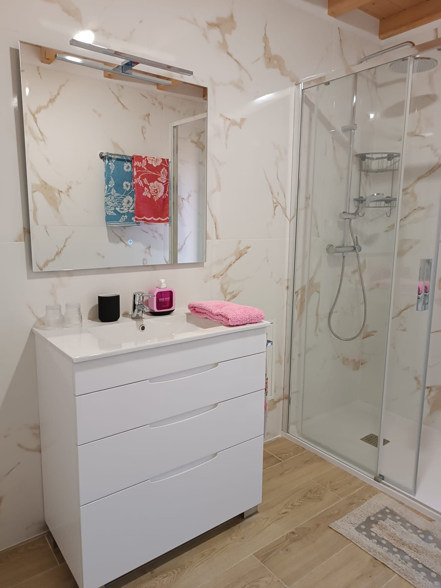 A bathroom with a white vanity, a glass shower enclosure, and a marble-patterned wall.