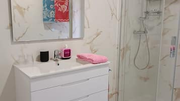 A bathroom with a white vanity, a glass shower enclosure, and a marble-patterned wall.