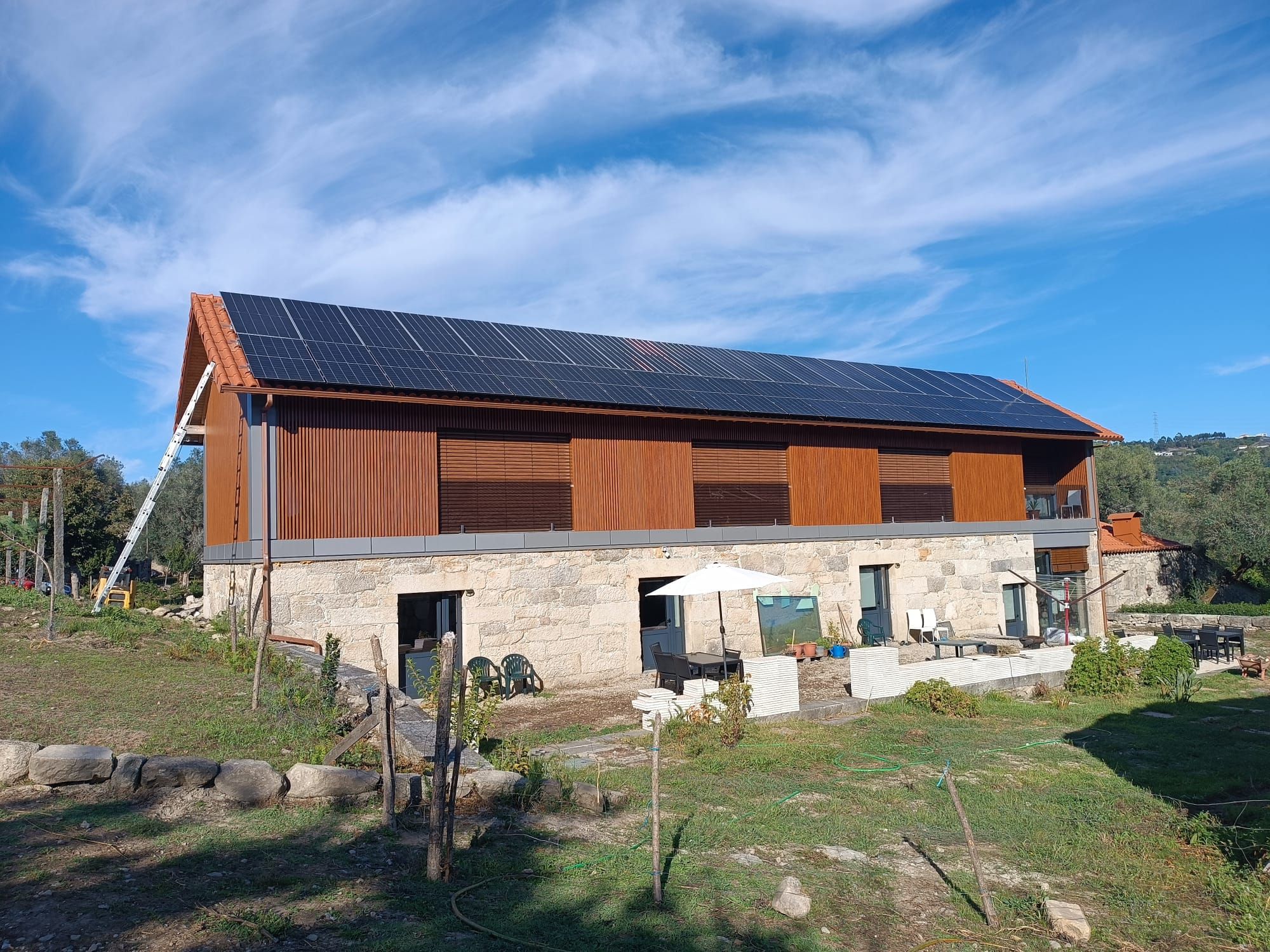 A modern two-story house with a sloped roof, solar panels, and a stone foundation.