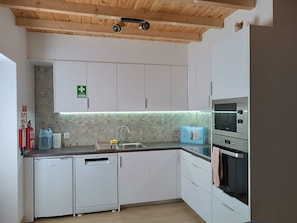 Cocina compacta con armarios blancos, pileta de acero inoxidable, horno integrado y salpicadero con diseño.