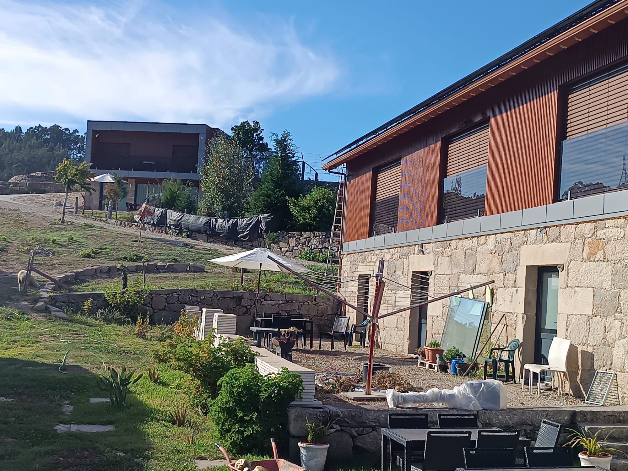 A modern building with a stone facade, outdoor seating area, and a view of a hill.