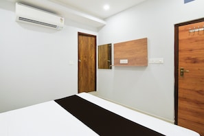 Ein Hotelzimmer mit einem Bett, einer Holztür, einer Wandklimaanlage und einem kleinen Regal.