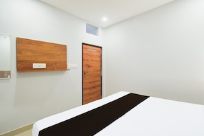 Ein Zimmer mit einem Bett, einer Holztür und einem an der Wand befestigten Regal mit einer Steckdose.