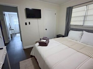A hotel room with a bed, a TV mounted on the wall, a desk with a chair, and a window with curtains. - You can bring everybody, have your own rooms, and still actually enjoy being together. (Montgomery)