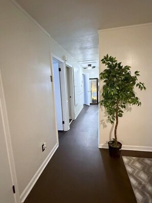 A hallway with white walls and a dark floor, leading to a door at the end. - You can bring everybody, have your own rooms, and still actually enjoy being together. (Montgomery)
