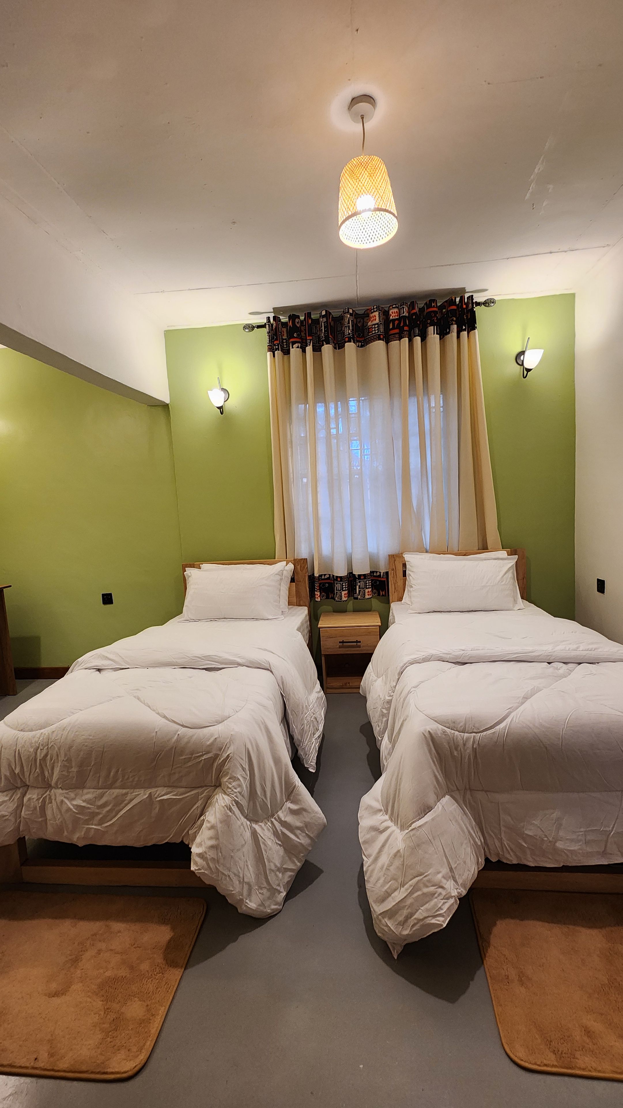 A hotel room with two beds, a ceiling light, and a window with curtains.