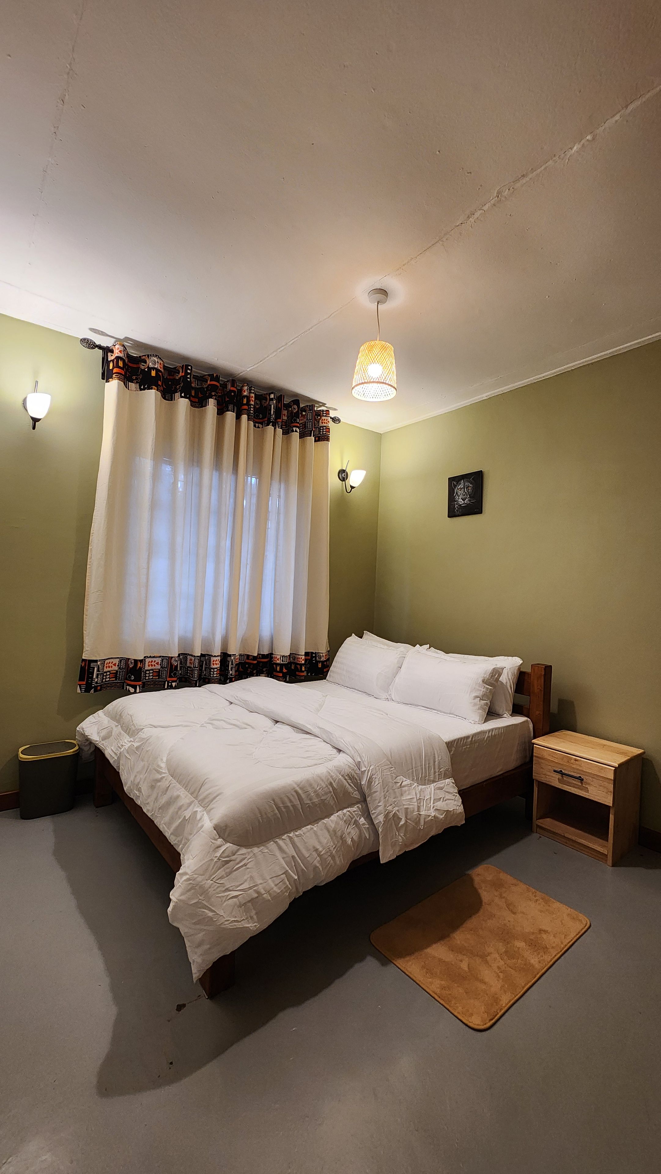 A bedroom with a bed, curtains, a nightstand, and a floor lamp.