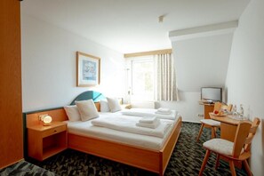 Een hotelkamer met een bed, nachtkastje, televisie en een klein bureau met een stoel.