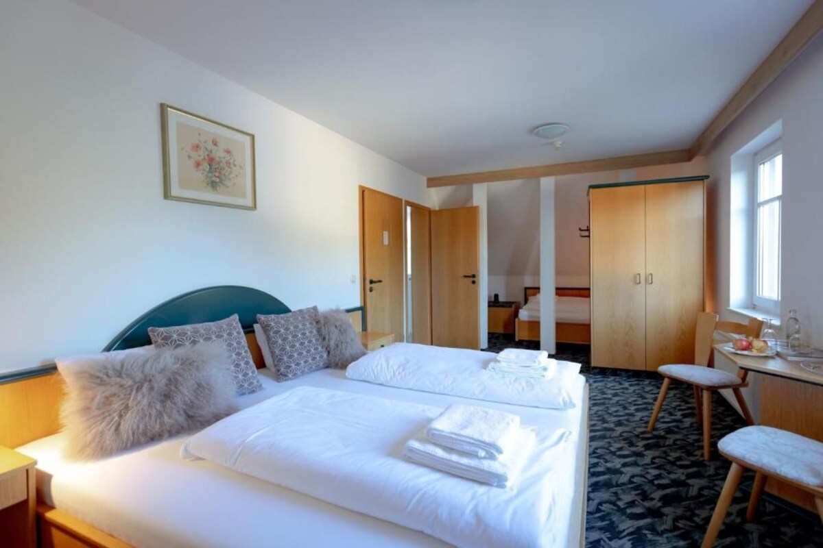 Een hotelkamer met een bed, bureau en stoel. Aan de muur hangt een schilderij en een raam zorgt voor daglicht.