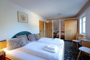 Een hotelkamer met een bed, bureau en stoel. Aan de muur hangt een schilderij en een raam zorgt voor daglicht.
