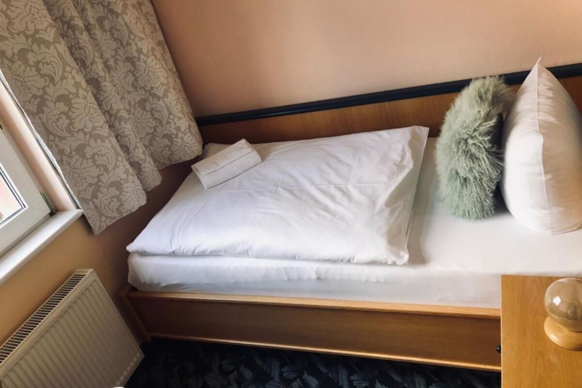 Een bed met witte lakens, een houten hoofdbord en een decoratief kussen.