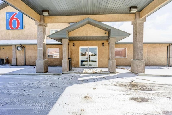 A motel with a covered entrance, a number '6' sign, and a view of the parking area. - Motel 6 Innisfail AB (Innisfail)