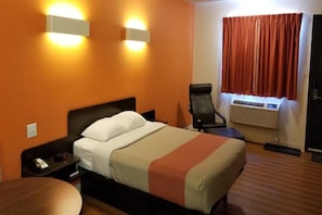 A hotel room with a bed, bedside table, chair, and an air conditioning unit. - Motel 6 Innisfail AB (Innisfail)