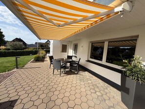 Une terrasse avec des carreaux hexagonaux, une table avec des chaises et un auvent à rayures.