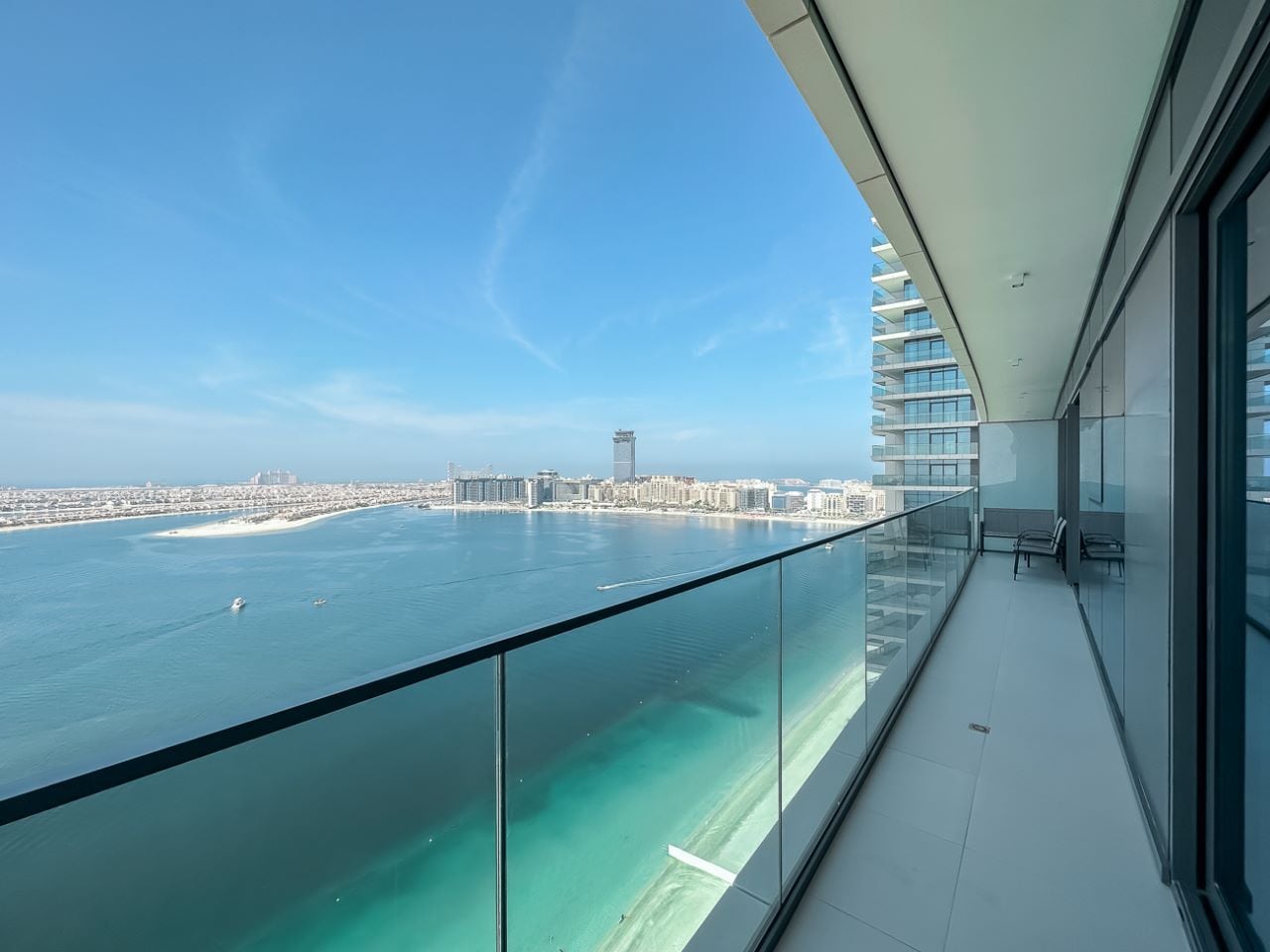 A balcony with a glass railing overlooking a body of water and a cityscape.