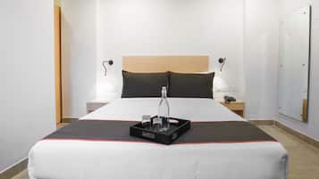 Een hotelkamer met een groot bed, nachtkastjes, een spiegel en een dienblad met een fles en glazen.
