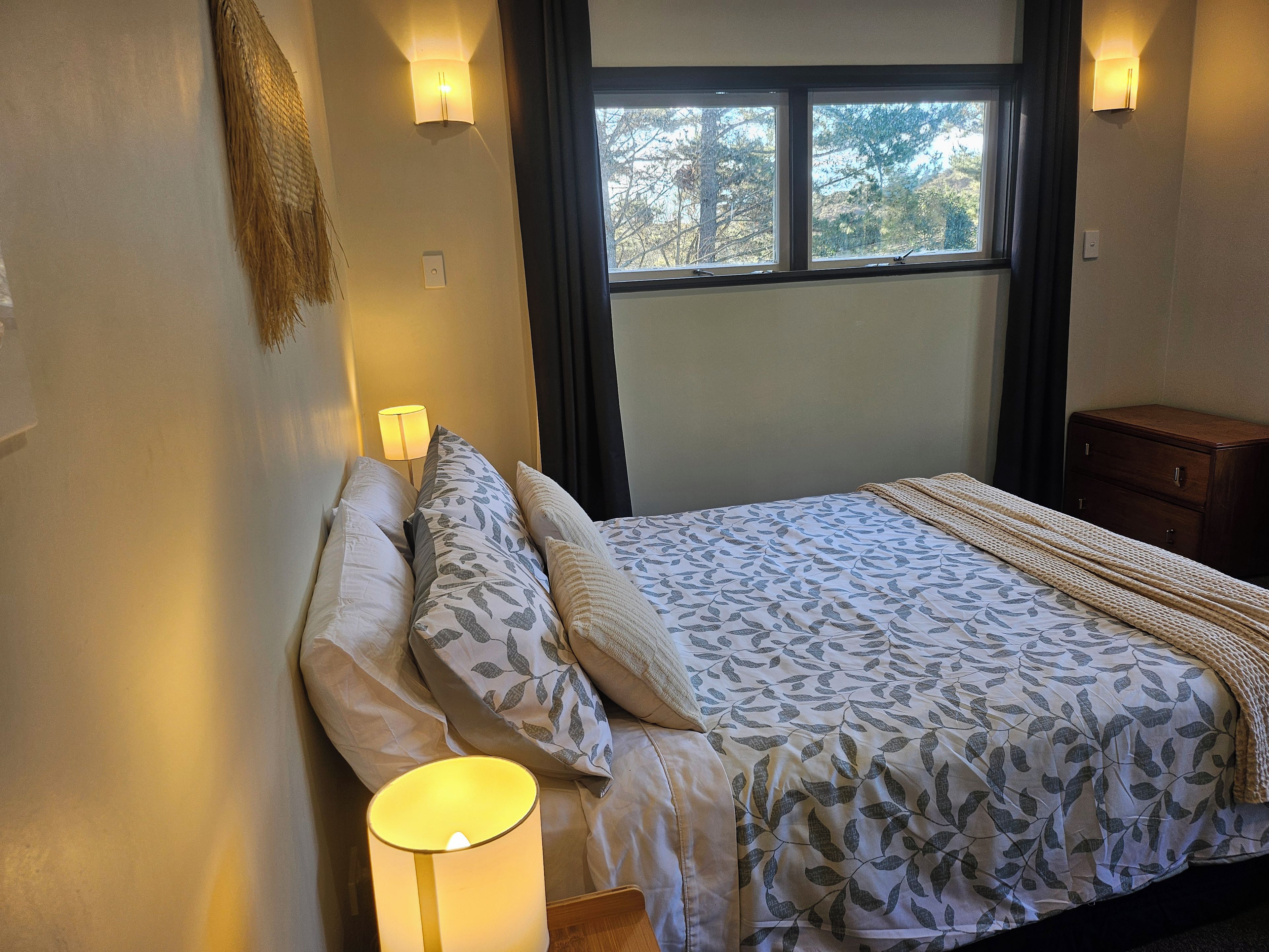 A bedroom with a bed, bedside lamps, a window, and a nightstand.