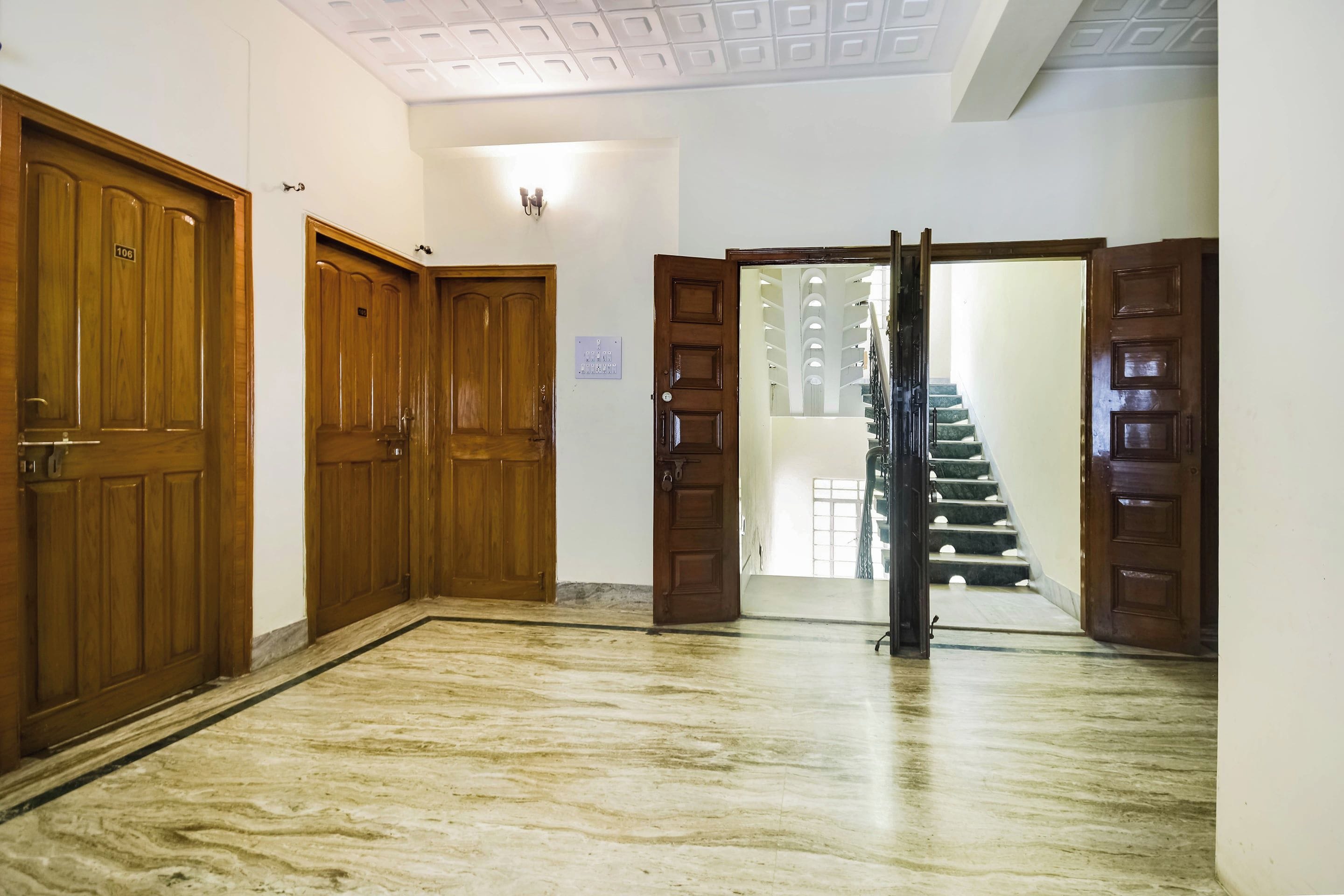 A hallway with wooden doors, a marble floor, and a staircase leading to an upper level.