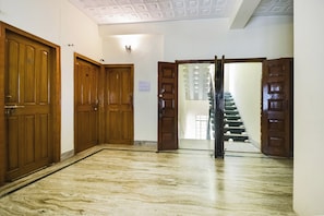A hallway with wooden doors, a marble floor, and a staircase leading to an upper level. - Collection O Karunamoyee Salt Lake (Barasat)