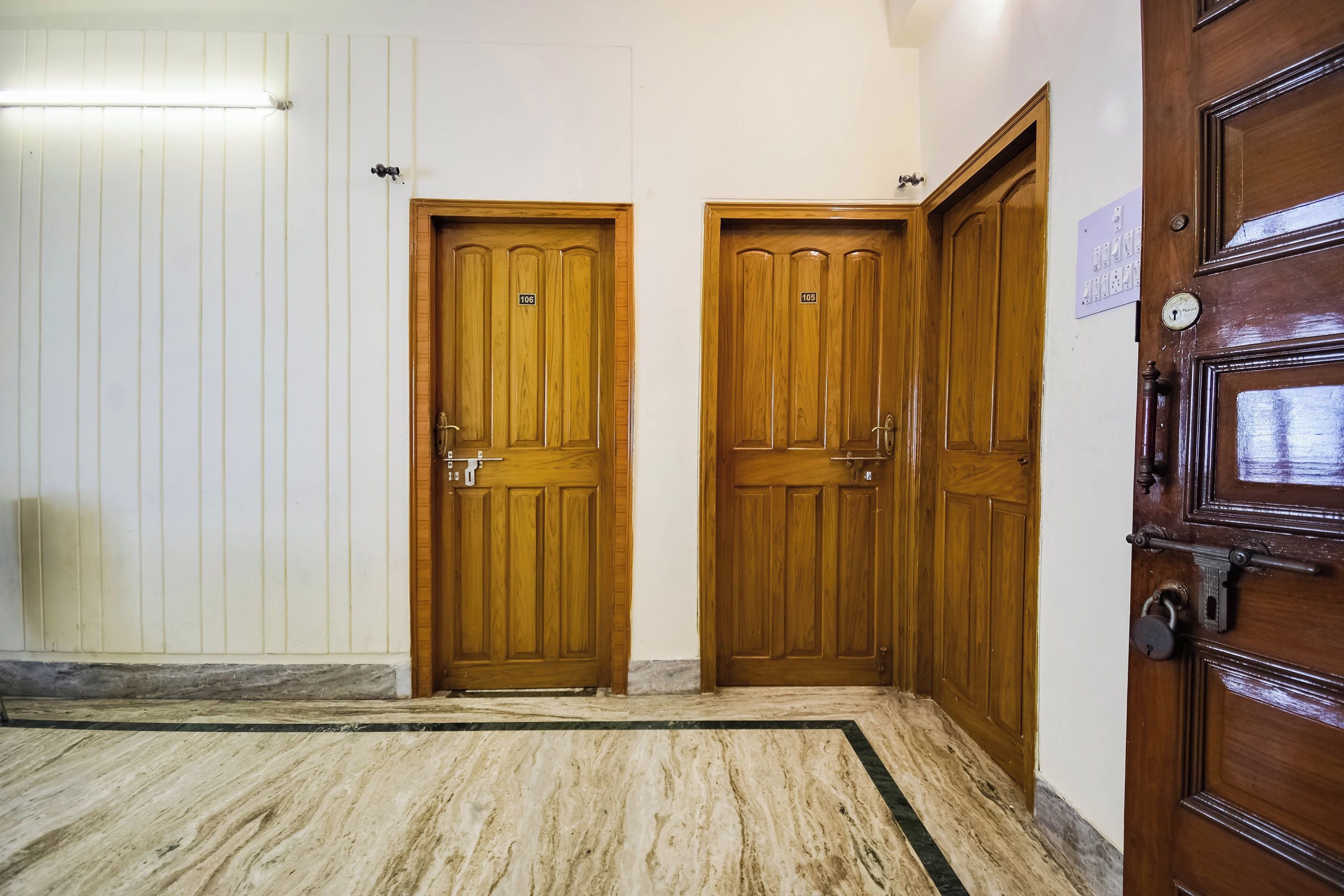 A hallway with two wooden doors, each with a number plate, and a marble-tiled floor.