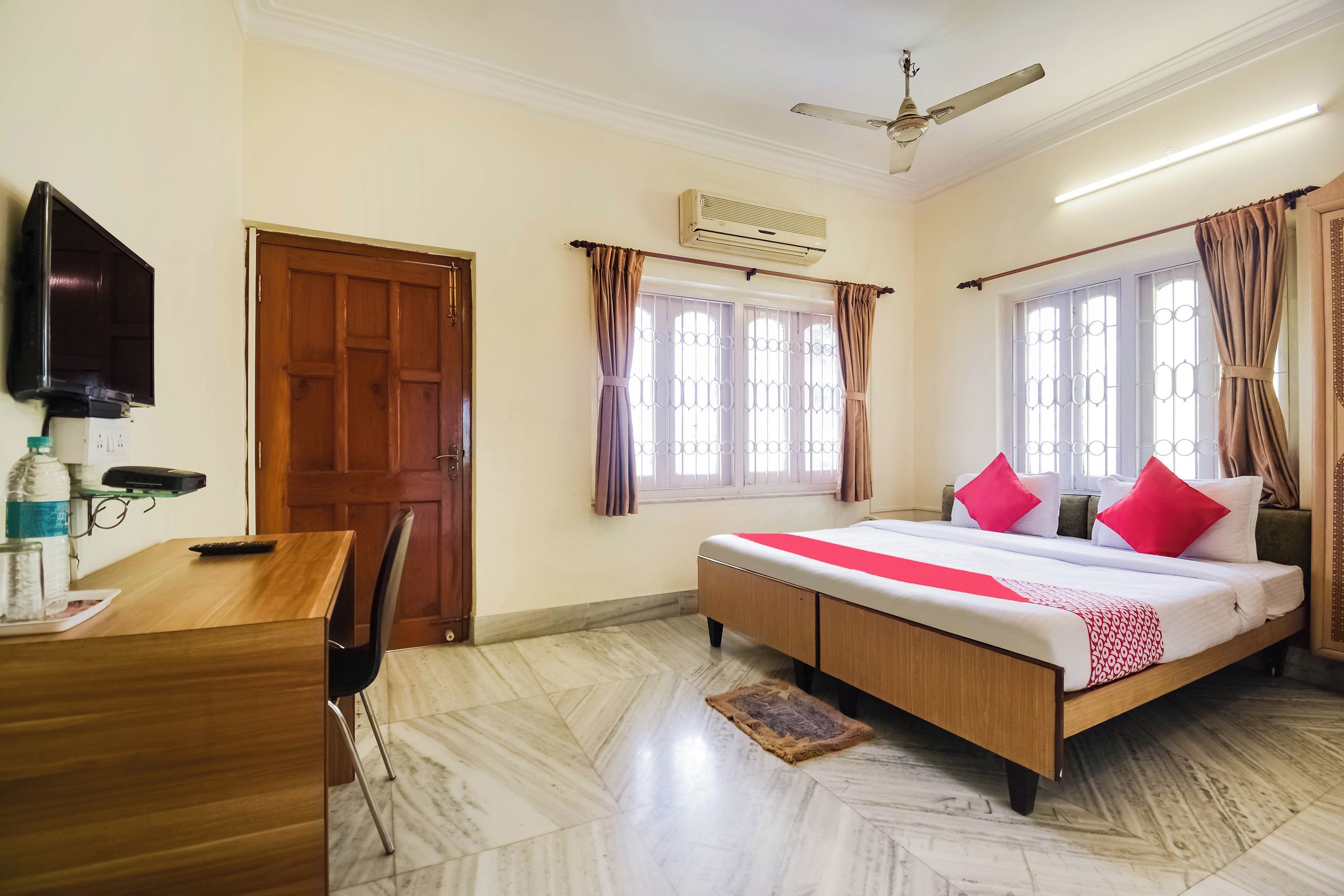 Une chambre d’hôtel équipée d’un lit, d’un bureau, d’une chaise, d’une télévision et d’un ventilateur de plafond.