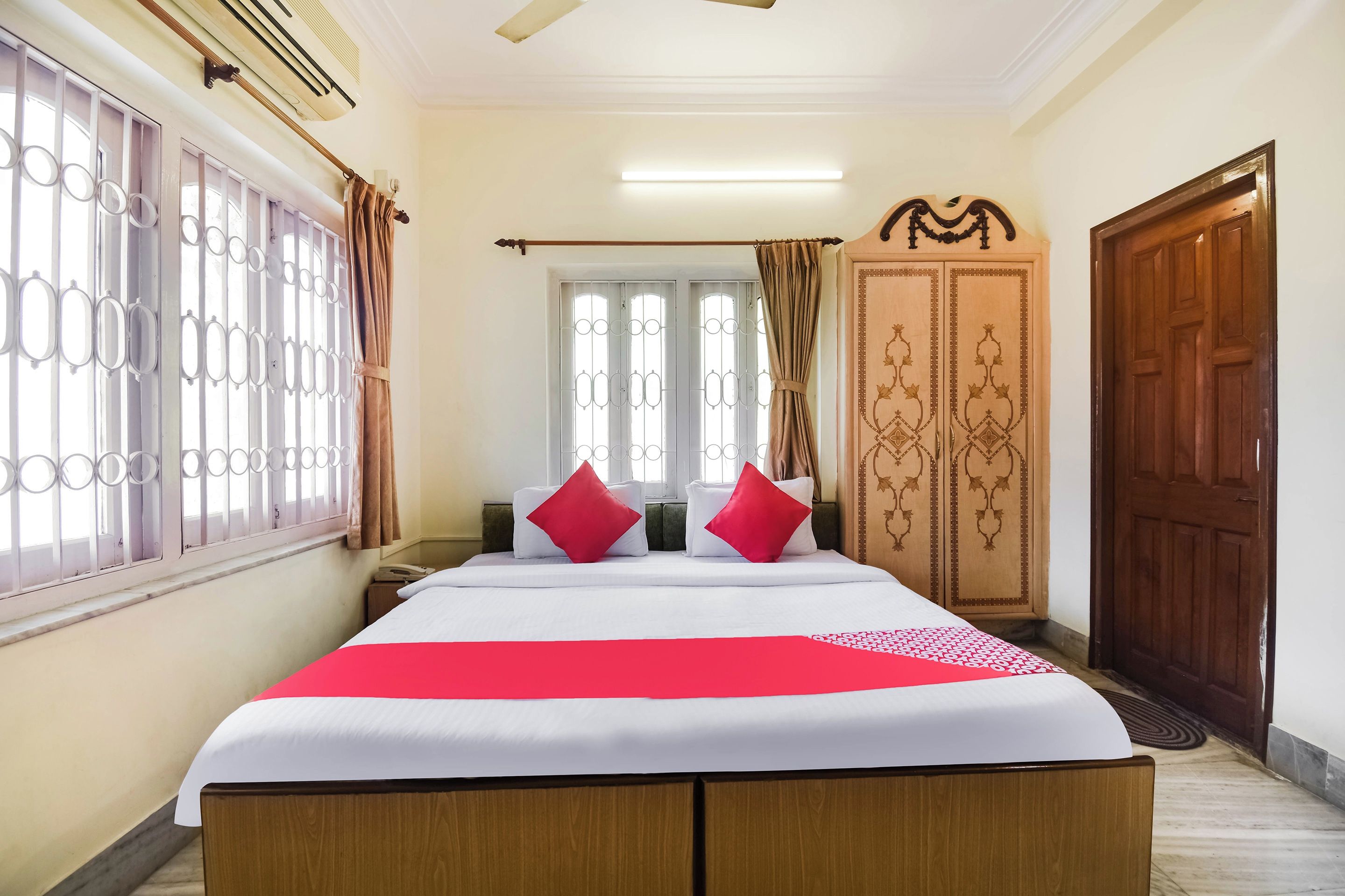 A hotel room with a bed, curtains, a wardrobe, and a window with bars.