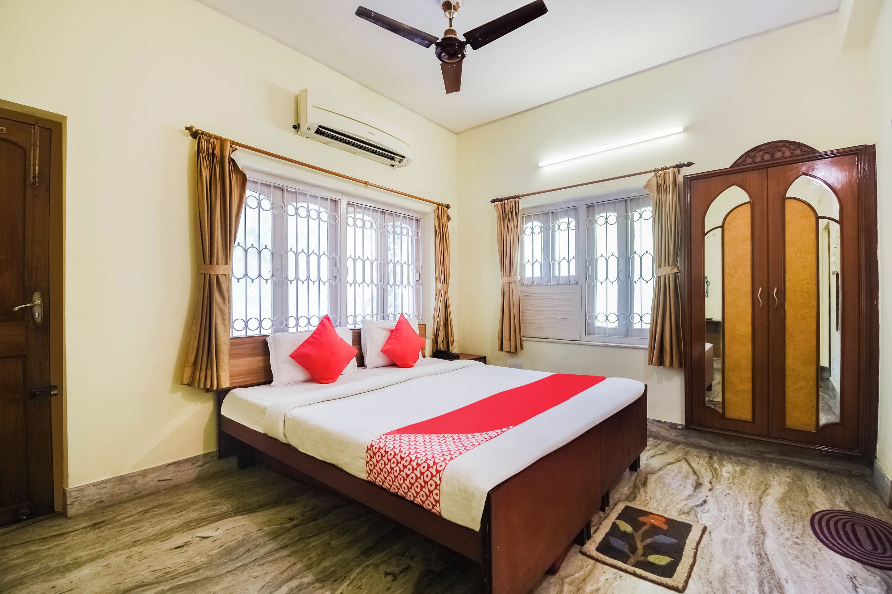 A bedroom with a bed, curtains, a ceiling fan, an air conditioning unit, and a wardrobe.