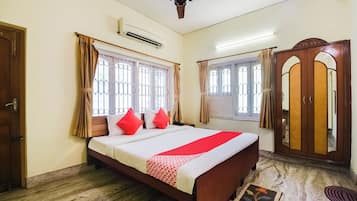 A bedroom with a bed, curtains, a ceiling fan, an air conditioning unit, and a wardrobe.