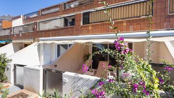 Un edificio residencial con balcón, zona de estar cubierta al aire libre y jardín con flores moradas.