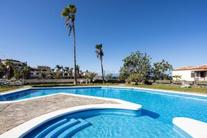 Une piscine à l’eau d’un bleu cristallin, entourée de palmiers, avec en arrière-plan une vue sur des bâtiments.