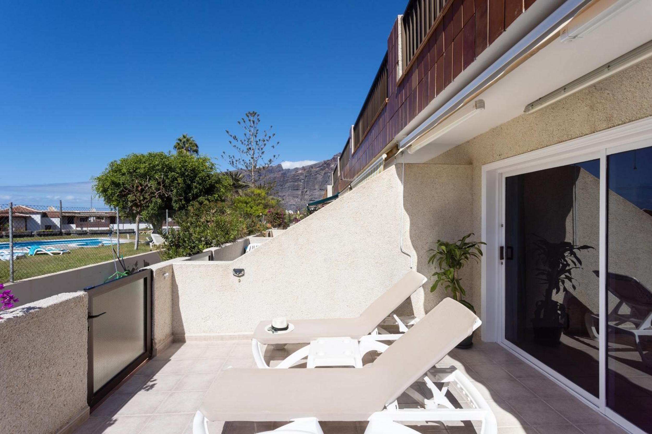A sunlit outdoor patio with lounge chairs, a pool, and a mountain view.