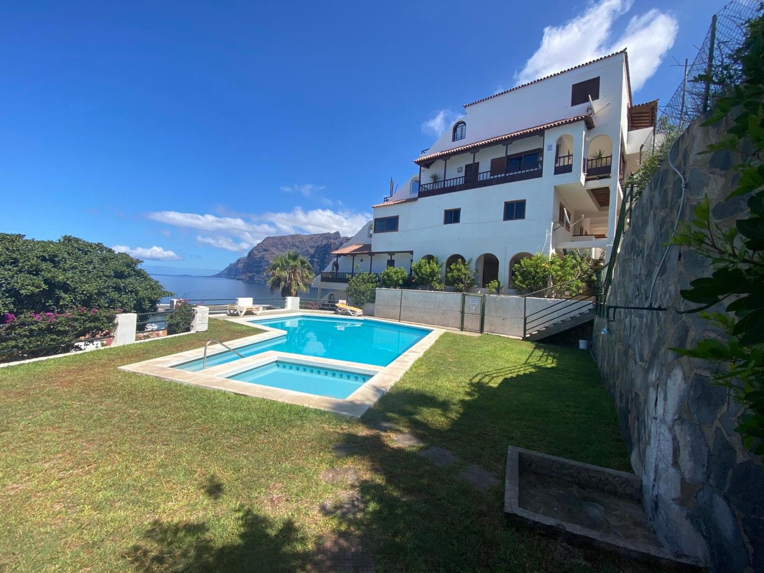 Ein zweigeschossiges Gebäude mit Swimmingpool, einer Steinmauer und Blick aufs Meer.