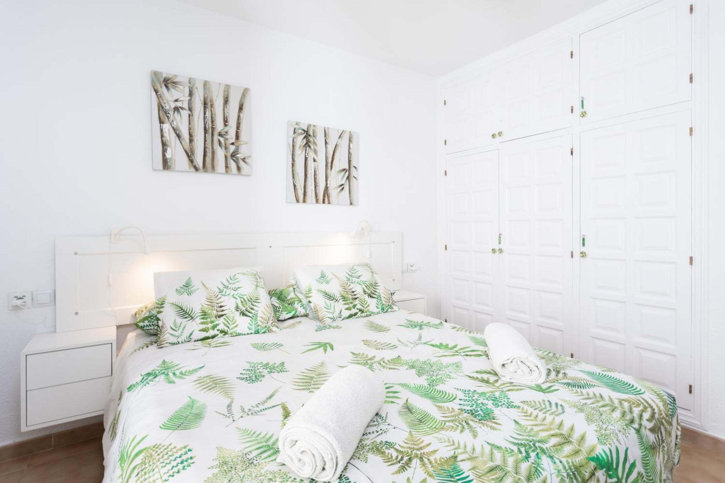 Une chambre à coucher avec un lit, deux tableaux accrochés au mur, une armoire et une table de chevet.