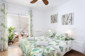 Une chambre à coucher avec un lit, une table de chevet, un ventilateur de plafond et une vue sur l’extérieur.