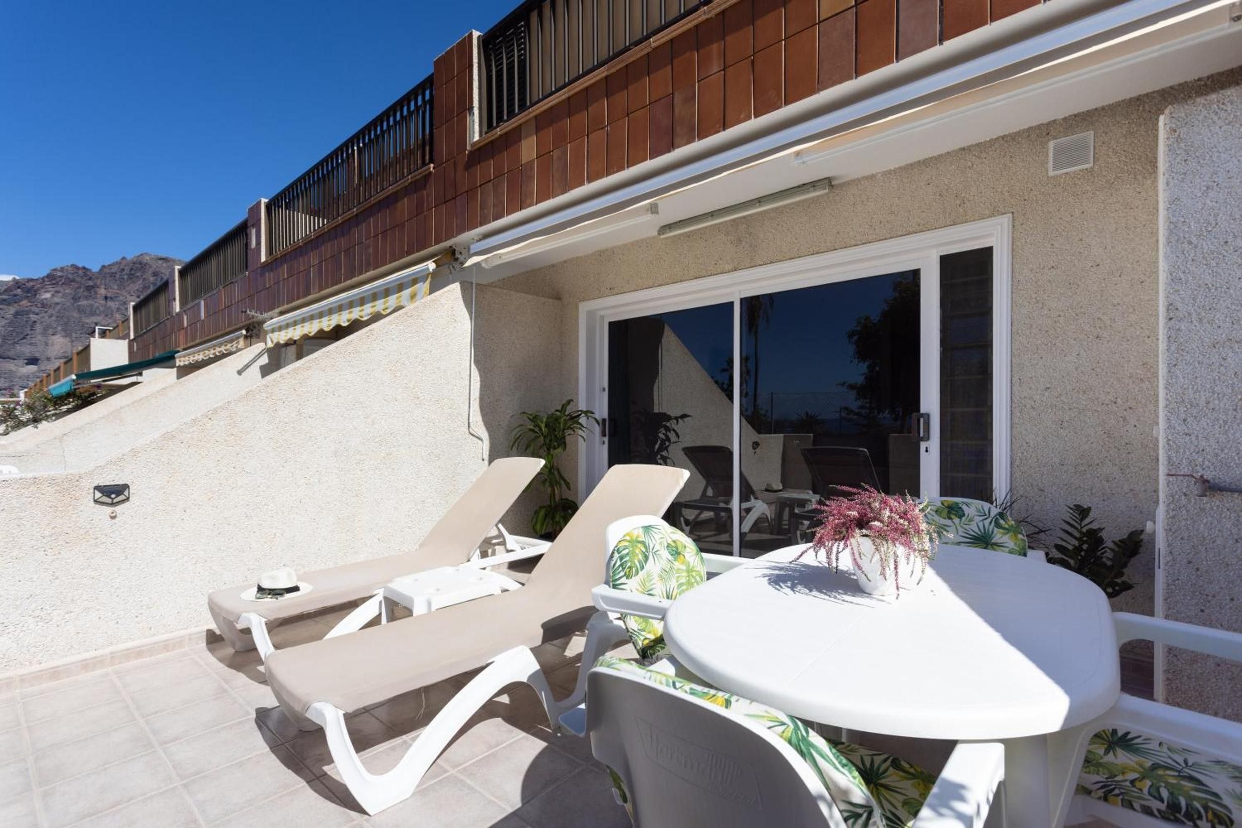 Une terrasse avec deux chaises longues et une table, une porte-fenêtre coulissante et une vue sur les montagnes en arrière-plan.