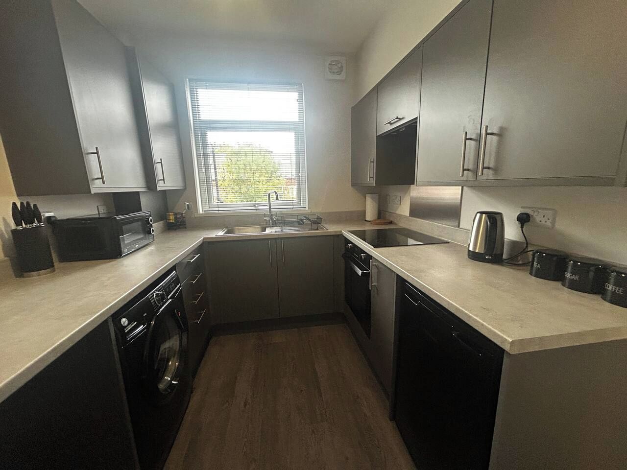 A modern kitchen with a dishwasher, oven, sink, and a window providing natural light.