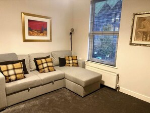 Un salon d’angle avec un canapé d’angle gris, un radiateur et deux œuvres d’art encadrées accrochées aux murs.