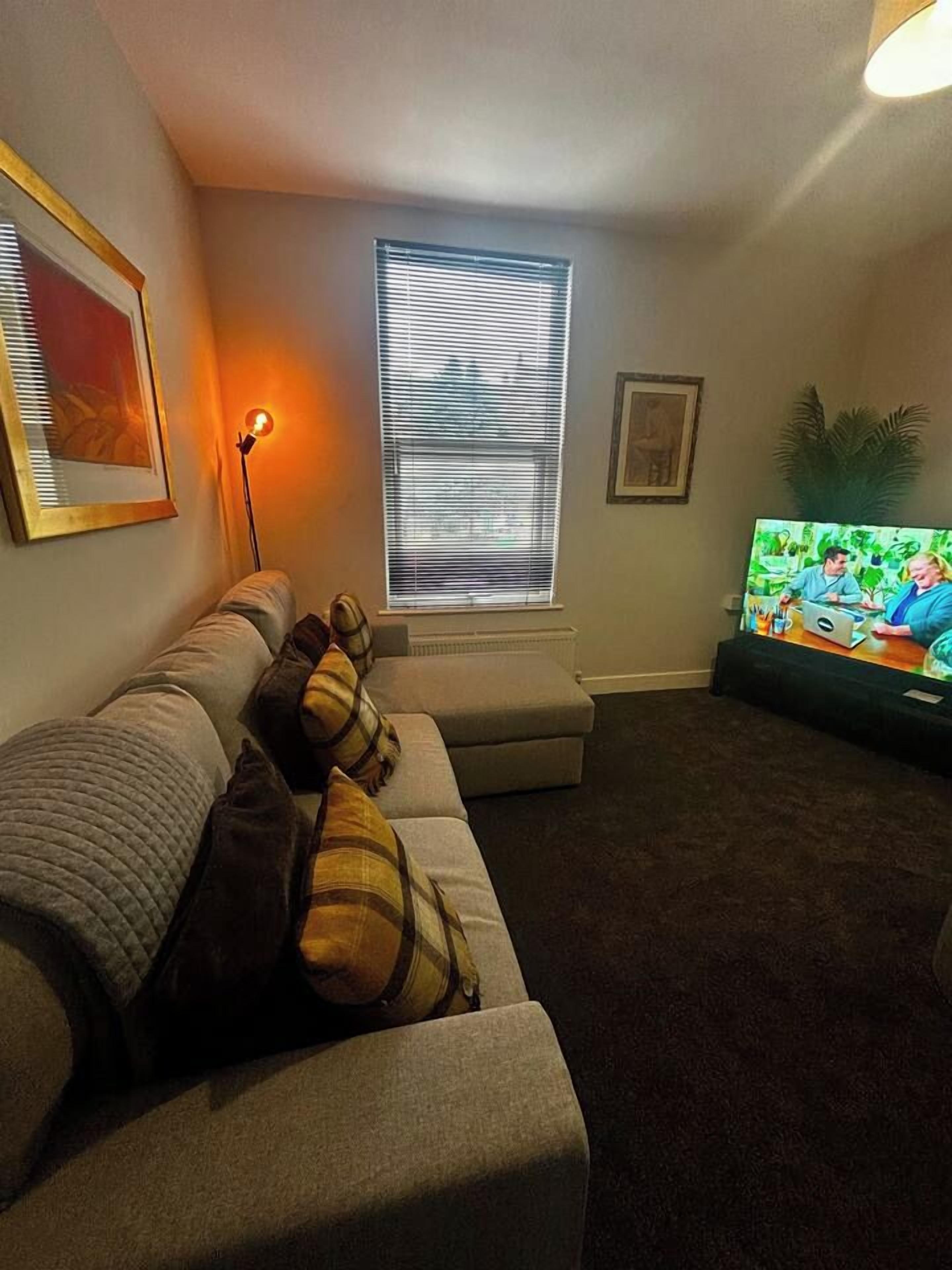 A living room with a couch, a television, and a window with blinds.