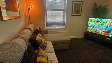 A living room with a couch, a television, and a window with blinds.