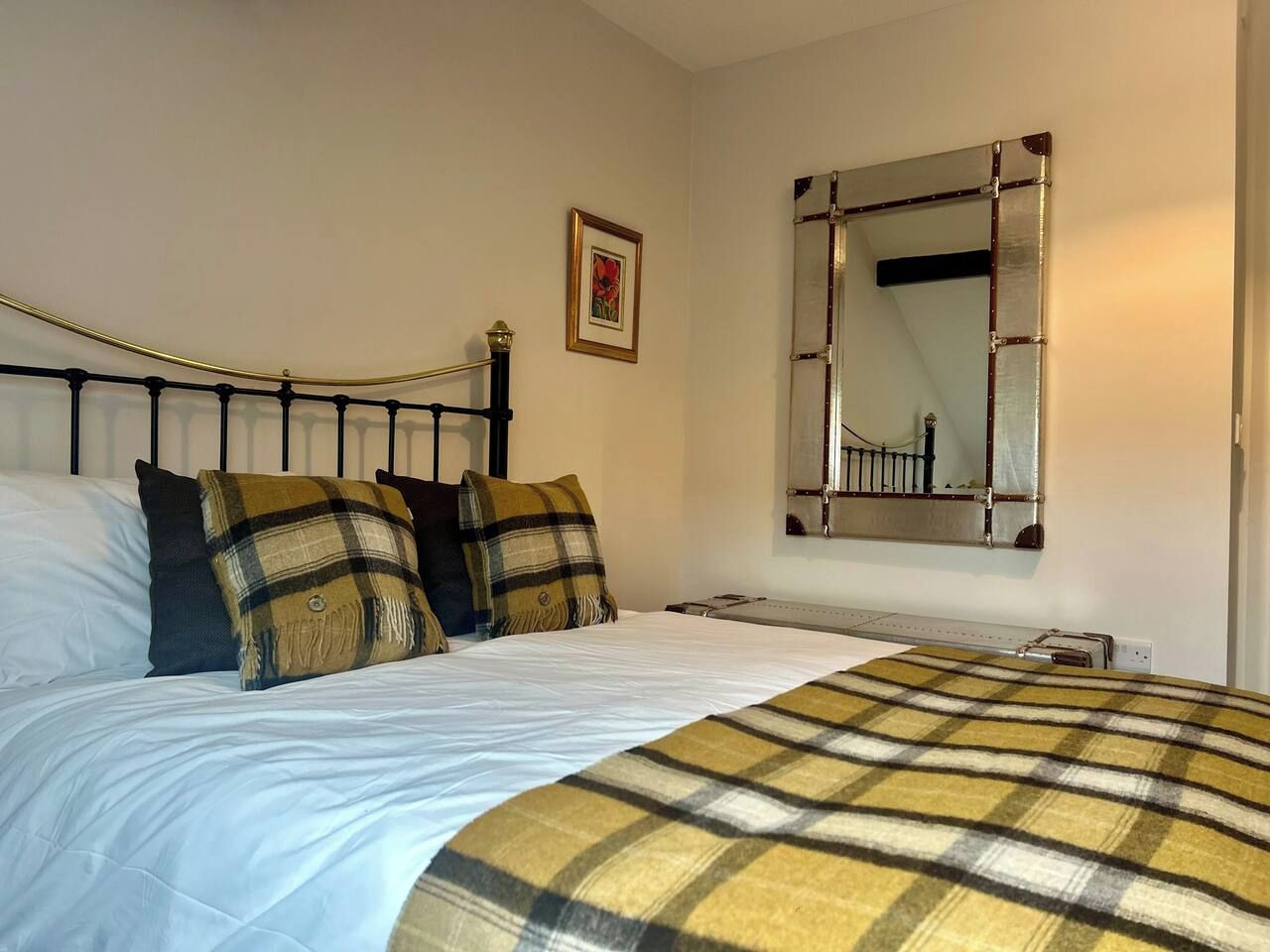 A bed with a headboard, a bedside table, a mirror, and a framed picture on the wall.
