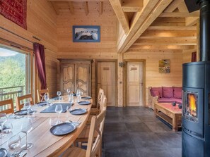 Un interior de madera con una mesa de comedor preparada para cuatro personas, un sofá y un estufa de leña.