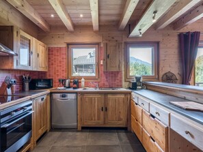 Une cuisine avec des meubles en bois, un lave-vaisselle, une cuisinière et une fenêtre donnant sur une maison.