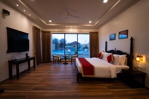 A hotel room with a bed, a TV, a desk, and a view of an outdoor swimming pool. - Jawai Zinc Journey By The Fern, Jawai (Pali)