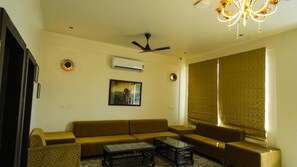 A living room with a sofa set, a coffee table, a ceiling fan, an air conditioning unit, and a large window with blinds. - Jawai Zinc Journey By The Fern, Jawai (Pali)