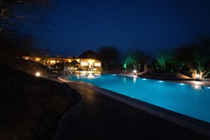 Un área de piscina iluminada de noche, con una casa al fondo.
