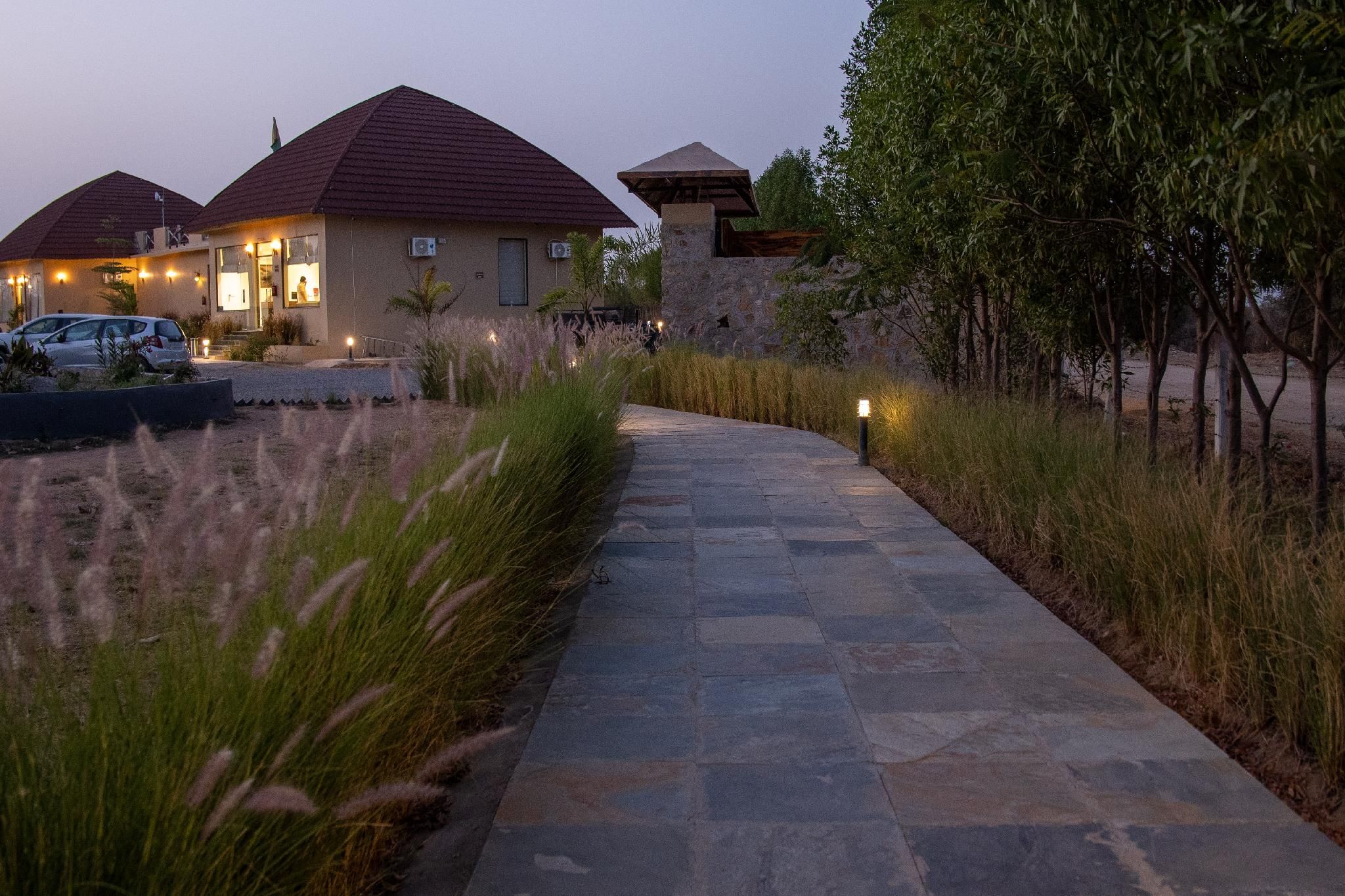 A pathway leading to a building with a stone facade and a red roof, surrounded by tall grasses and trees.