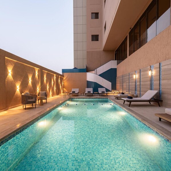 A swimming pool with lounge chairs and a wall with built-in lighting. - Braira Jazan Hotel (Jizan)