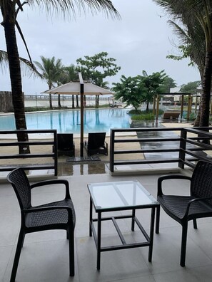 A poolside area with a glass table and chairs, a covered seating area, and a view of the pool. - The Tropics at Macarthur Park (Palo)